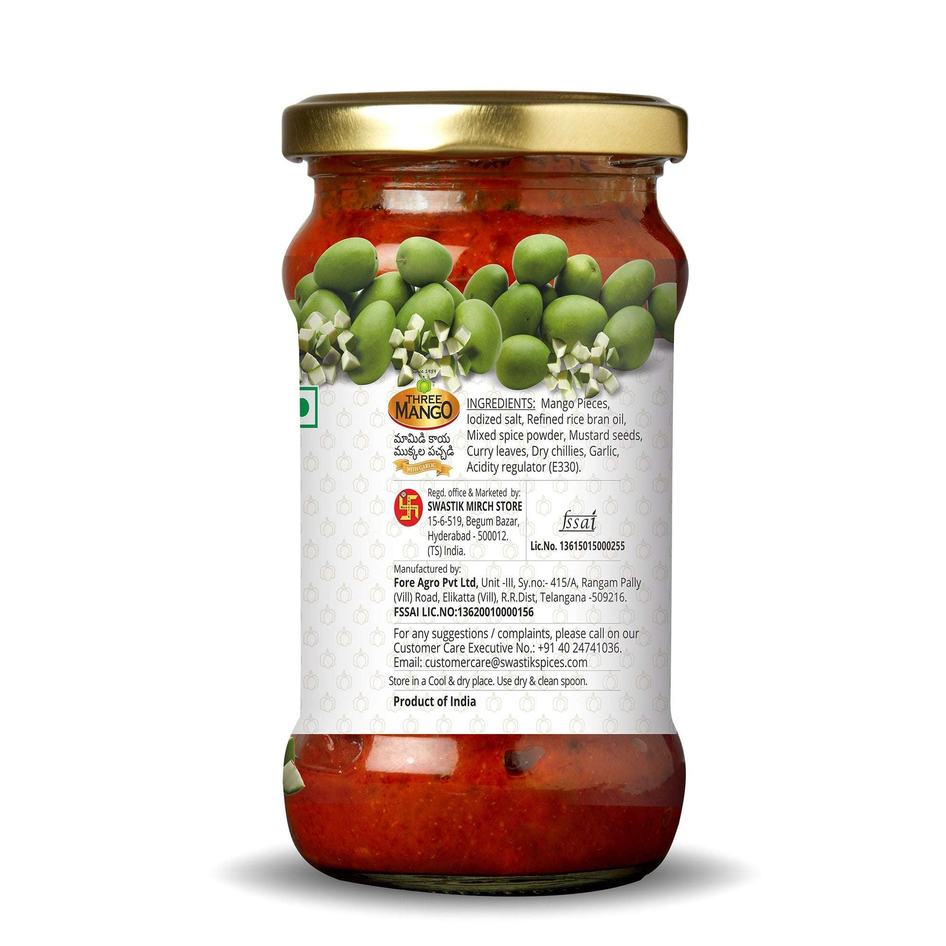 Back side of Three Mango mango pickle jar showing ingredients list, manufacturer details, FSSAI license, and quality assurance on white label with green mango graphics.
