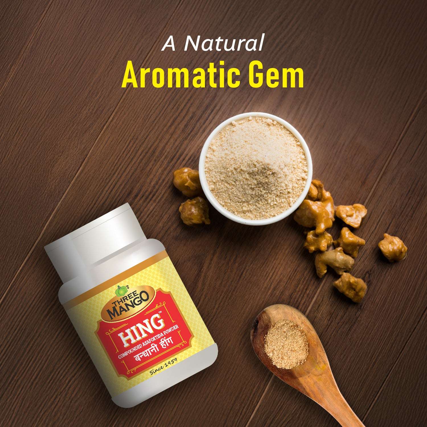 Hing powder in a bowl and wooden spoon with gum resin on a wooden surface next to Three Mango Hing container.